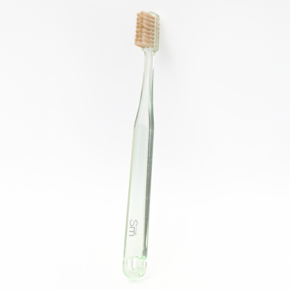 Green plastic toothbrush with brown bristles on a white background