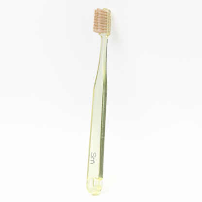 Yellow plastic toothbrush with brown bristles on a white background